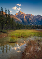 Beautiful mountain peak reflecting in a serene lake surrounded by forest at sunset