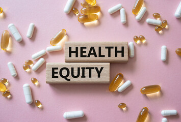 Health Equity symbol. Wooden blocks with words Health Equity. Beautiful pink background with pills. Medicine and Health Equity concept. Copy space.