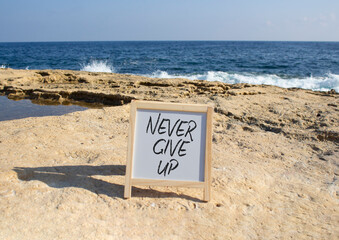 Never give up symbol. White Blackboard with Concept words Never give up. Beautiful sea background. Business and Never give up concept. Copy space.