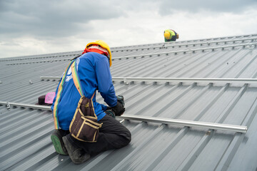 Builder mounting photovoltaic solar modules on roof of house. Back view of man engineer in helmet installing solar panel system outdoors. Concept of alternative and renewable energy.