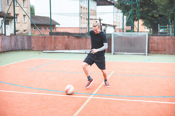 Young man focuses on controlling a football on an outdoor court. He carefully juggles the ball with precision, surrounded by an urban backdrop of buildings and a goal, combining sports and skill