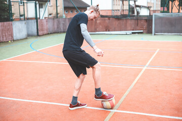 Young man focuses on controlling a football on an outdoor court. He carefully juggles the ball with precision, surrounded by an urban backdrop of buildings and a goal, combining sports and skill