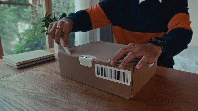 Cropped shot of anonymous guy in casualwear unboxing parcel with bar code at home table