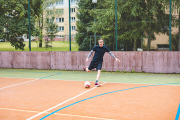 Young man performs a powerful football kick on an outdoor court, mid-motion with the ball in the...