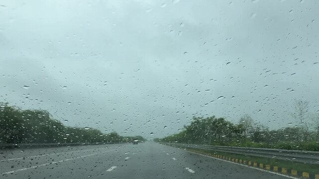 Heavy raining during monsoon and droplets textured on glass of moving car in the highway roads.