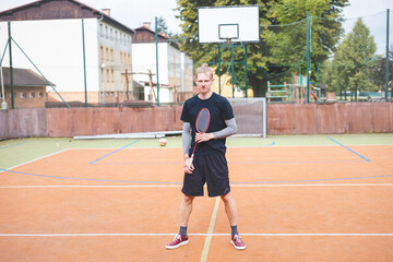 Obraz premium Badminton player focuses on the shuttlecock mid-air during a match on an outdoor court. With his racket raised, he prepares for the next shot, surrounded by an urban and scenic background