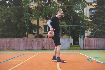 Obraz premium Basketball player controls and dribble the ball during a casual game on an outdoor court, bending down in focus. The court is surrounded by trees and nature, giving a peaceful and athletic atmosphere