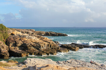 Rocky coastline landscape with blue ocean waves and cloudy sky