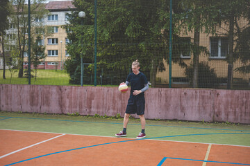 Fototapeta premium Basketball player controls and dribble the ball during a casual game on an outdoor court, bending down in focus. The court is surrounded by trees and nature, giving a peaceful and athletic atmosphere