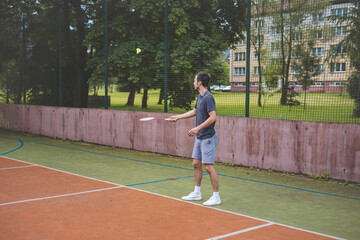 Obraz premium Badminton player focuses on the shuttlecock mid-air during a match on an outdoor court. With his racket raised, he prepares for the next shot, surrounded by an urban and scenic background
