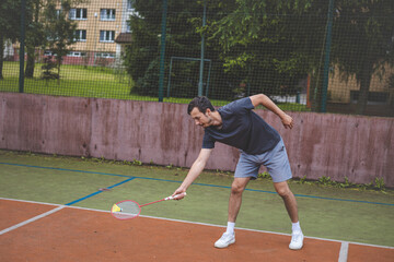 Badminton player focuses on the shuttlecock mid-air during a match on an outdoor court. With his...
