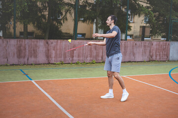 Badminton player focuses on the shuttlecock mid-air during a match on an outdoor court. With his...