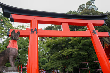 Large red Torii gate and fox statue under cloudy sky in Kyoto