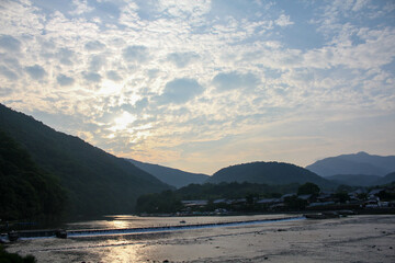 Wide river flowing past mountains under cloudy textured sky