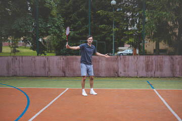 Badminton player focuses on the shuttlecock mid-air during a match on an outdoor court. With his racket raised, he prepares for the next shot, surrounded by an urban and scenic background