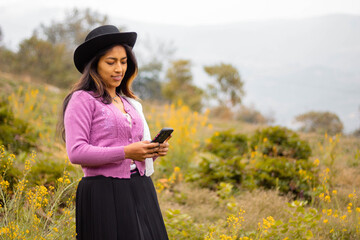 Foto de una feliz y bonita campesina con un sombrero hablando por un teléfono celular en los Andes peruanos. Mujer usando teléfono móvil
