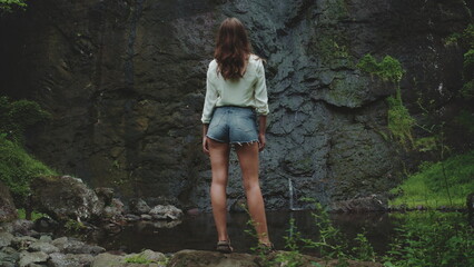 A woman stands in front of a majestic waterfall on the tropical islands of French Polynesia, surrounded by lush greenery and cascading water.