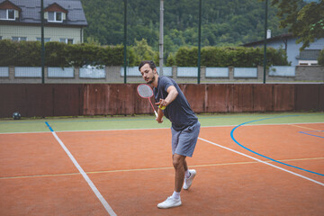 Badminton player focuses on the shuttlecock mid-air during a match on an outdoor court. With his...