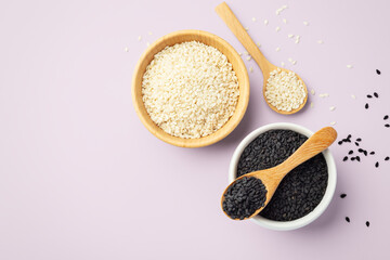 Black sesame seeds in white bowl with wood spoon and white sesame in wooden bowl isolated on pink background