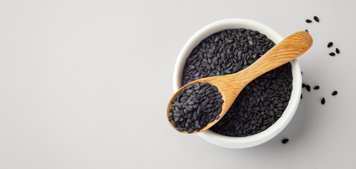 Black sesame in wooden spoon and white bowl on beige table, top view