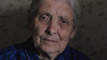 Portrait of old elderly gray haired grandmother woman with deep wrinkles on face sitting at nursing home, calm looking in camera. Suffers from nervous tic tremor or Parkinson, trembling eyelid