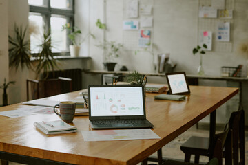 Naklejka premium Wooden table with laptop, tablet and paper with diagrams and schemes in modern it office