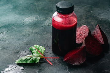 Fresh squeezed beet juice in bottle among leaves and beetroot chunks, selective focus, copy space