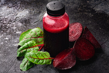 Fresh squeezed beet juice in bottle among leaves and beetroot chunks, selective focus, copy space