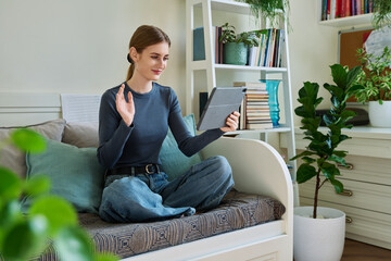 Teenage female student at home looking talking in web camera of digital tablet