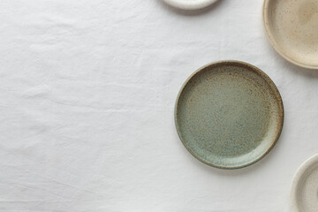 Empty rustic vintage plates dinnerware on a white tablecloth with copy space as a background for meal food dishes, food mock up