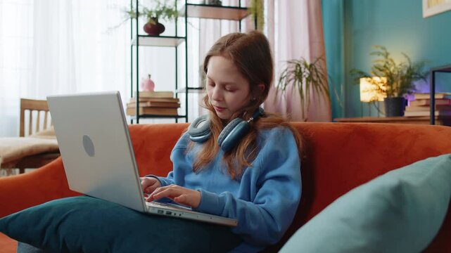 Overtired Caucasian young girl bored using laptop while sitting on sofa at home. Sleepy teenage child cannot concentrate on work and types lazily. Female preteen is not interested in doing a project.