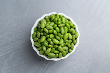 Fresh edamame soybeans in bowl on grey textured table, top view
