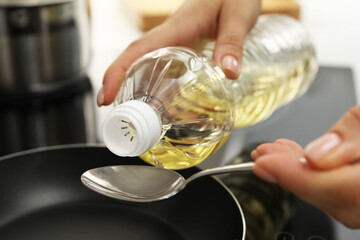 Woman with bottle of oil and spoon in kitchen, closeup