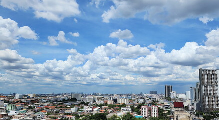 Scenery of a city under bright blue sky. The view of the capital city is seen from a tall building. View of houses, tall buildings, big trees on a bright summer day. The sky has scattered clouds. 
