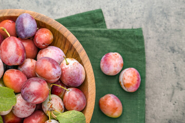 Ripe plums in bowl on grey textured table, flat lay