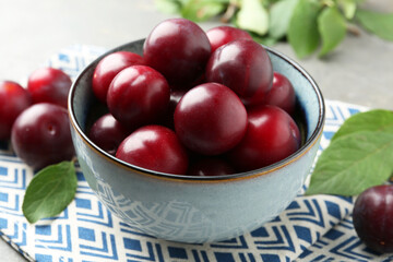 Tasty ripe plums in bowl on grey table, closeup