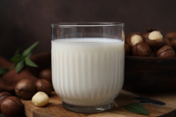 Glass of macadamia milk and nuts on wooden table, closeup