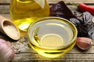Cooking oil in bowl and products on wooden table, closeup