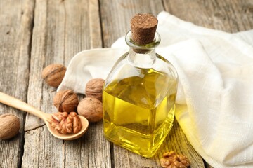 Cooking oil in bottle, spoon and walnuts on wooden table, closeup