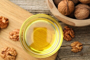 Cooking oil in bowl and walnuts on wooden table, flat lay