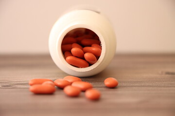 Orange pills with a white bottle on a wooden table with white background.