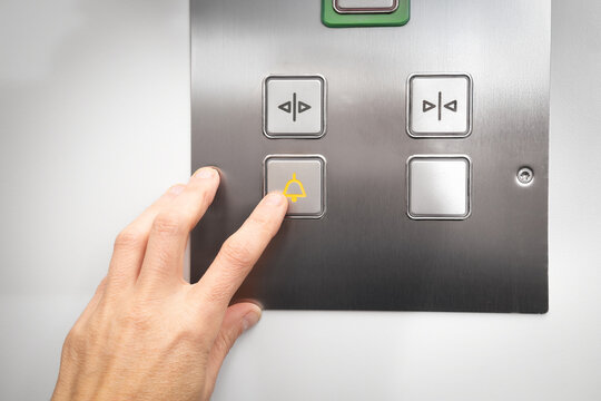Elevator emergency call button used by passenger. Close up of woman pushing a button with a bell icon on stainless steel intercom. Call for help or stuck elevator in building. Selective focus.