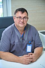 Medicr, wearing gray scrubs and a name badge, smiles confidently