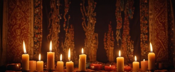 A row of lit candles in various sizes and colors stands against a dark background with intricate patterns and designs