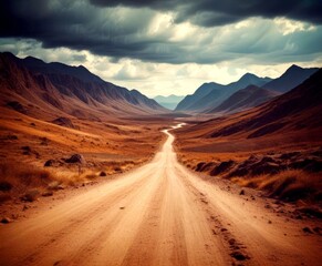 A winding dirt road stretches through a vast, arid desert landscape, flanked by rugged mountains under a dramatic cloudy sky