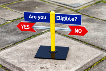 Metal pole with a sign on top has two arrows pointing in opposite directions, each labeled with the text word "YES" and "NO" against question "ARE YOU ELIGIBLE"