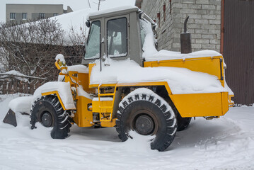 A bulldozer for clearing roads of snow during a snowfall. A bulldozer with large wheels for road construction works stands in a snowdrift in winter. Road equipment.