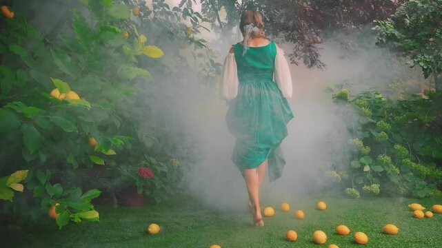 silhouette beauty Happy fantasy woman harvesting lemons in garden trees walking in fog back rear view. Sexy old style green dress, girl model. Citrus fruits lemon orange lying on ground grass lawn 4k