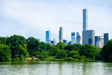 Fototapeta premium Big Lake in Central Park in New York, with people sailing on boats, and the New York skyline in the background