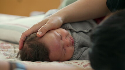Close-up of a sleeping baby in a cozy bed, with a gentle hand caressing the infant's head, capturing a moment of peace, comfort, and security in a warm and loving home